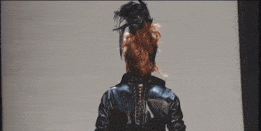 a woman wearing a black leather jacket and feathered hat