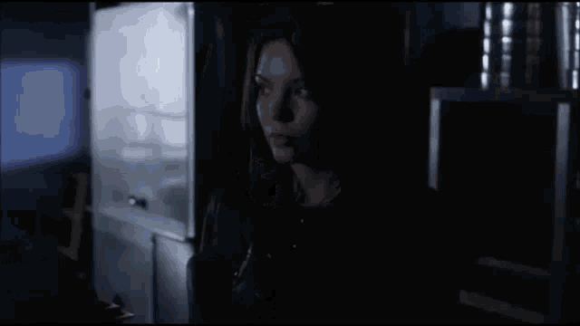 a woman standing in a dark room with a shelf in the background