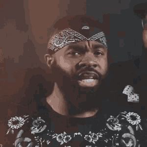 a man with a bandana on his head is making a funny face while another man says `` so good '' .