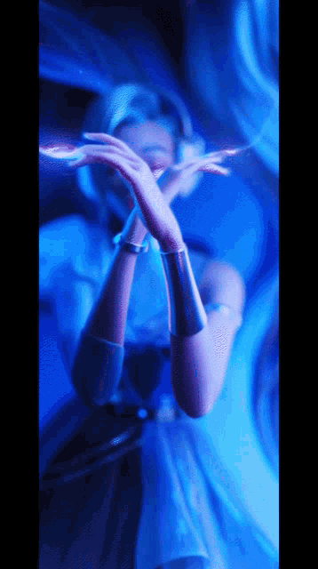 a woman in a blue dress holds her hands up in front of her face