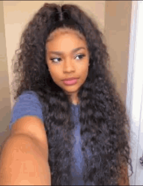 a woman with long curly hair is taking a selfie with her phone .