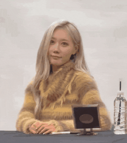 a woman sitting at a table with a bottle of water and a mirror