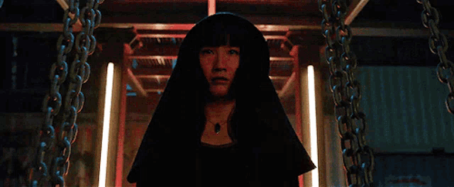 a woman in a black robe is standing in a dark room with chains hanging from the ceiling
