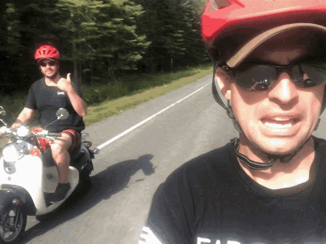 a man wearing a red helmet is riding a scooter next to a man wearing sunglasses