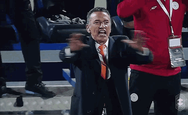 a man in a suit and orange tie is screaming in a stadium