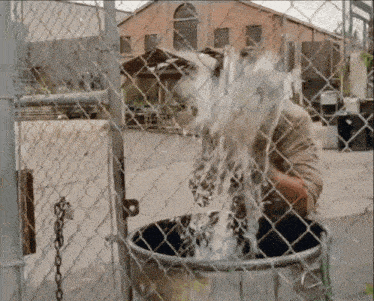 a man is pouring water into a bucket behind a chain link fence