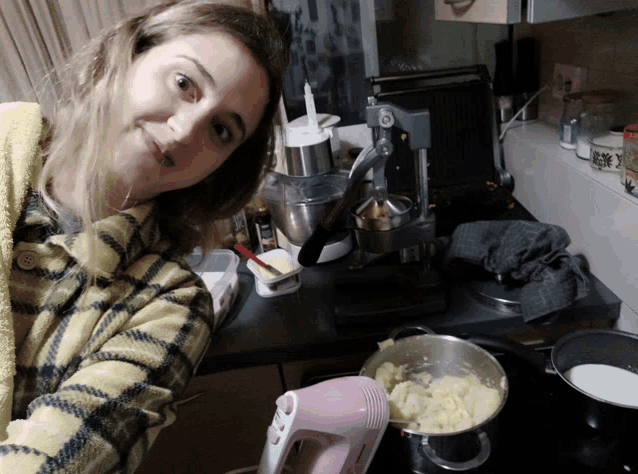 a woman in a yellow plaid shirt is smiling in front of a pink mixer
