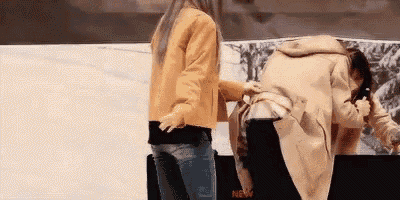 two women are standing next to each other in front of a white wall . one of the women is wearing a yellow jacket .