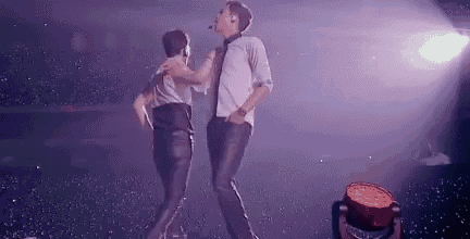 two men are dancing on a stage in a dark room .