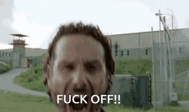 a man with a beard is screaming and saying `` fuck off '' in front of a building .
