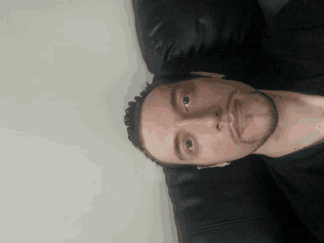 a man with a beard is laying down on a black leather couch