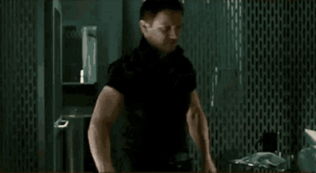 a man in a black shirt is standing in a bathroom with his arms up .