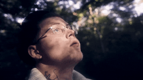 a man wearing glasses and a tattoo on his neck looks up at the sky