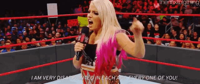 a woman in a wrestling ring is holding a microphone and screaming .
