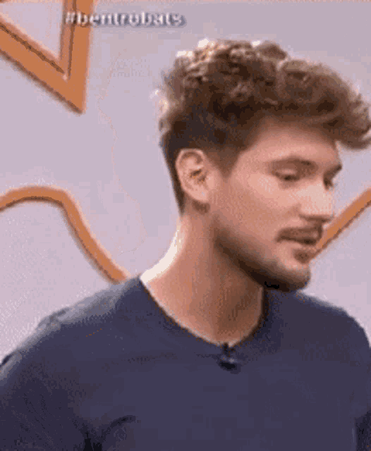 a man with a beard is wearing a blue shirt and has a microphone on his neck .