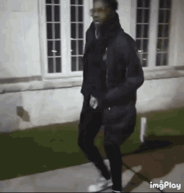 a man in a black jacket is walking down a sidewalk .