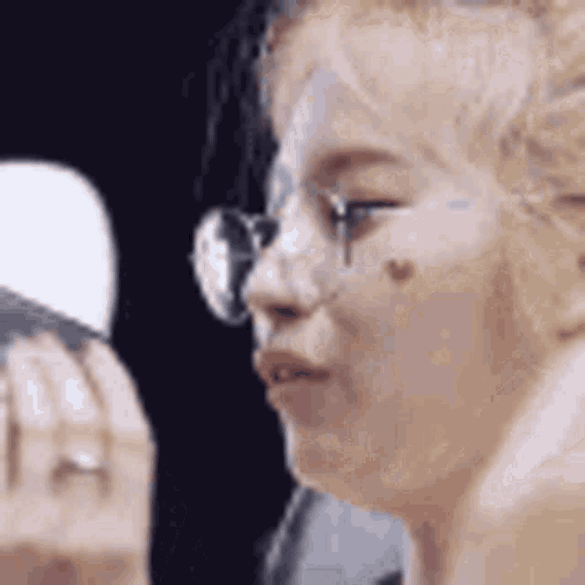 a woman wearing glasses is looking at herself in the mirror .