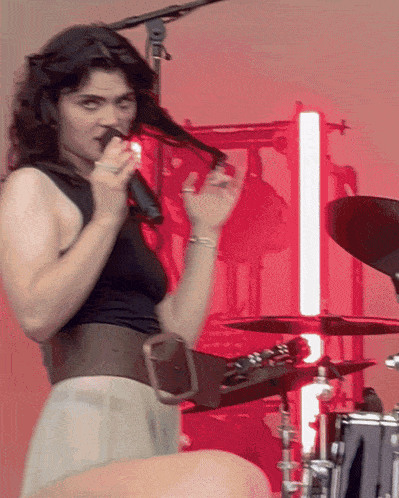 a woman singing into a microphone with a red light behind her