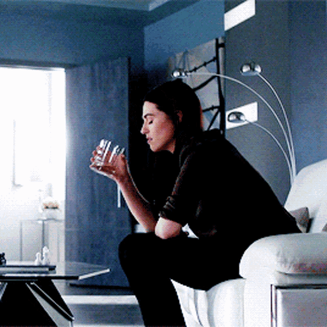 a woman sitting on a couch holding a glass of water