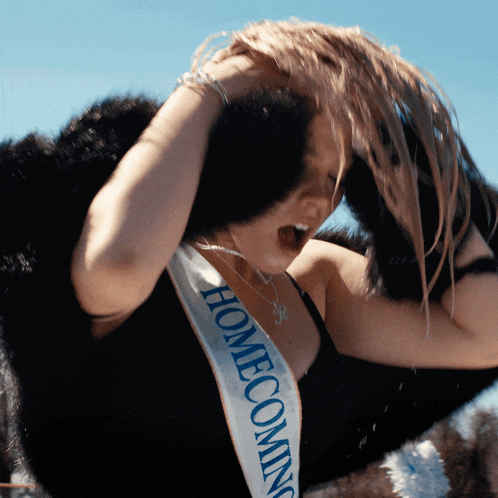 a woman wearing a homecoming sash holds her hair