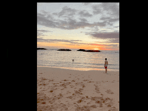 a man in red shorts stands on a beach watching the sunset