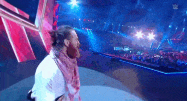 a man is standing on a stage in front of a crowd at a wrestling event .