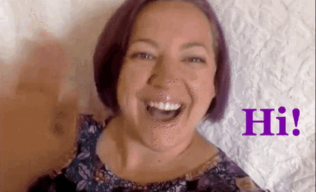 a woman with purple hair is smiling and says hi in purple letters