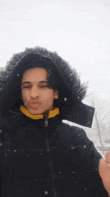 a young man wearing a black jacket with a fur hood blows a kiss