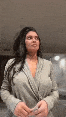 a woman in a gray robe is standing in a room looking up .