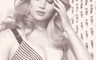 a woman in a striped bra is standing in front of a wall with a pattern on it .