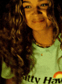 a woman with curly hair wearing a shirt that says kitty hawaii