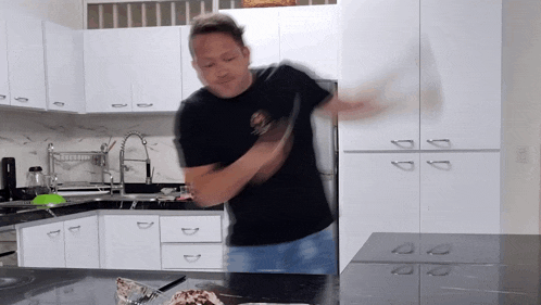 a man in a black shirt is standing in a kitchen with white cabinets