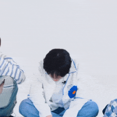 a boy with a blue flower on his jacket is sitting on the floor and giving the middle finger