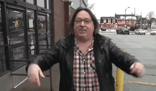a man wearing a plaid shirt and a black jacket is standing in front of a store