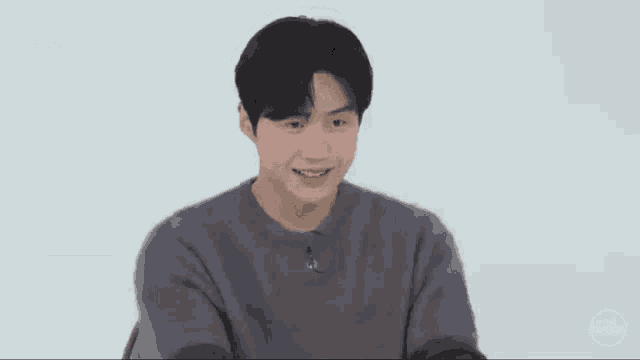 a young man wearing a grey sweater is smiling and making a funny face .