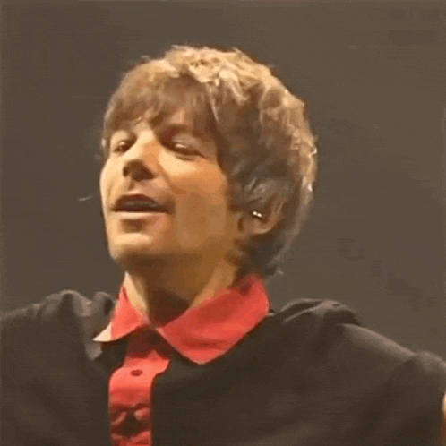 a close up of a man wearing a black jacket and a red collared shirt .