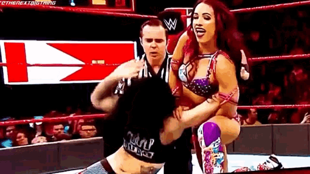 two women are wrestling in a wrestling ring with a referee in the background .
