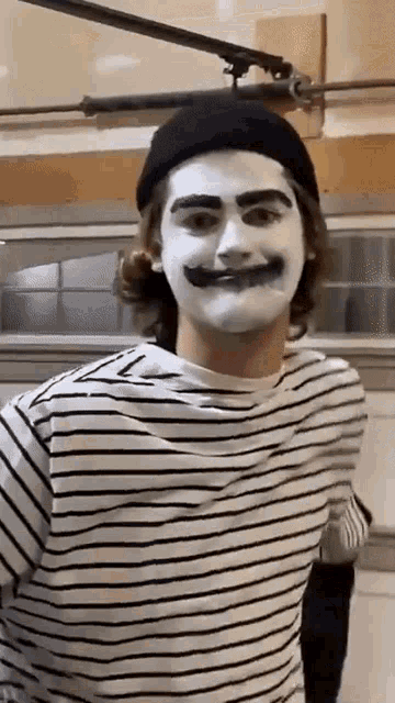 a man wearing a striped shirt and a black hat is dressed as a mime with white paint on his face .