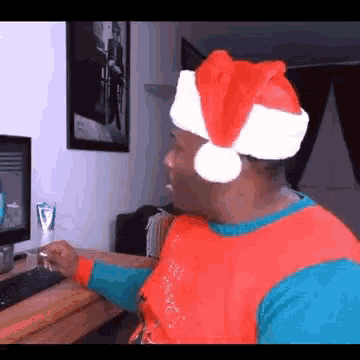 a man wearing a santa hat is looking at a computer screen .