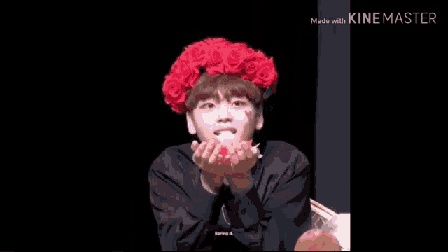 a young man wearing a red flower crown is blowing petals in the air .