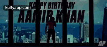 a man is standing in front of a city with the words happy birthday aamir khan written on it .