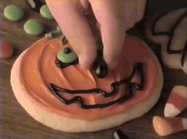 a person decorates a cookie with a pumpkin face