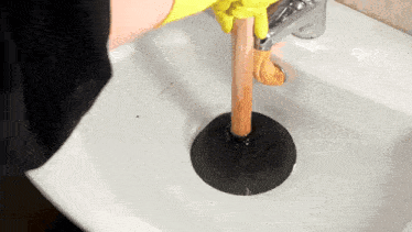 a person is using a wooden plunger to unblock a sink .