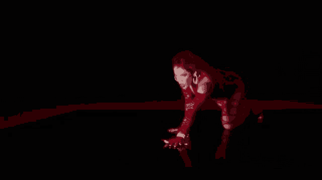 a woman in a red dress is kneeling down on the floor in a dark room .