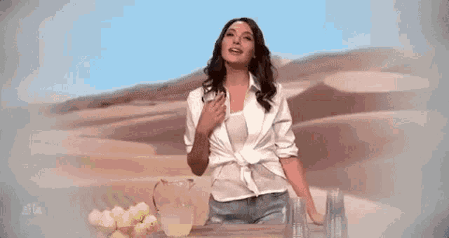 a woman in a white shirt and jeans is standing in front of a pitcher of lemonade in the desert .