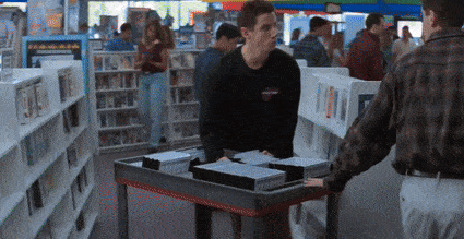 a man in a harley davidson shirt pushes a cart full of dvds in a store