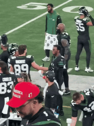 a man wearing a red america again hat shakes hands with a group of football players
