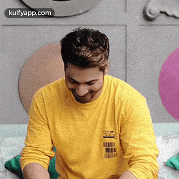a man wearing a yellow shirt is sitting on a bed with balloons in the background .