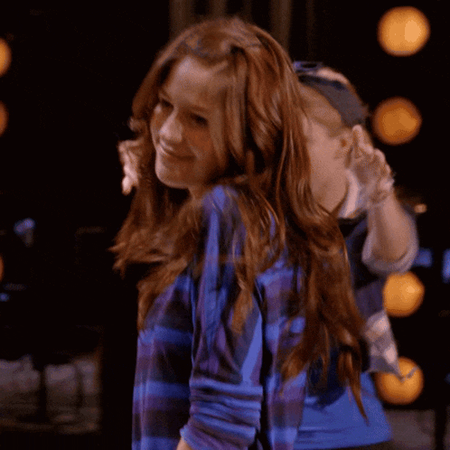 a woman in a blue striped shirt smiles in front of another woman