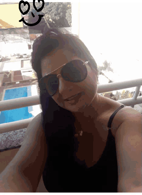 a woman wearing sunglasses is taking a selfie with a smiley face drawn on her head